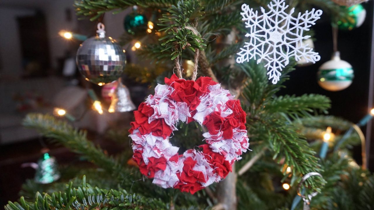 Mini rag rug wreath hanging from a Christmas tree in red and white candy cane stripes.