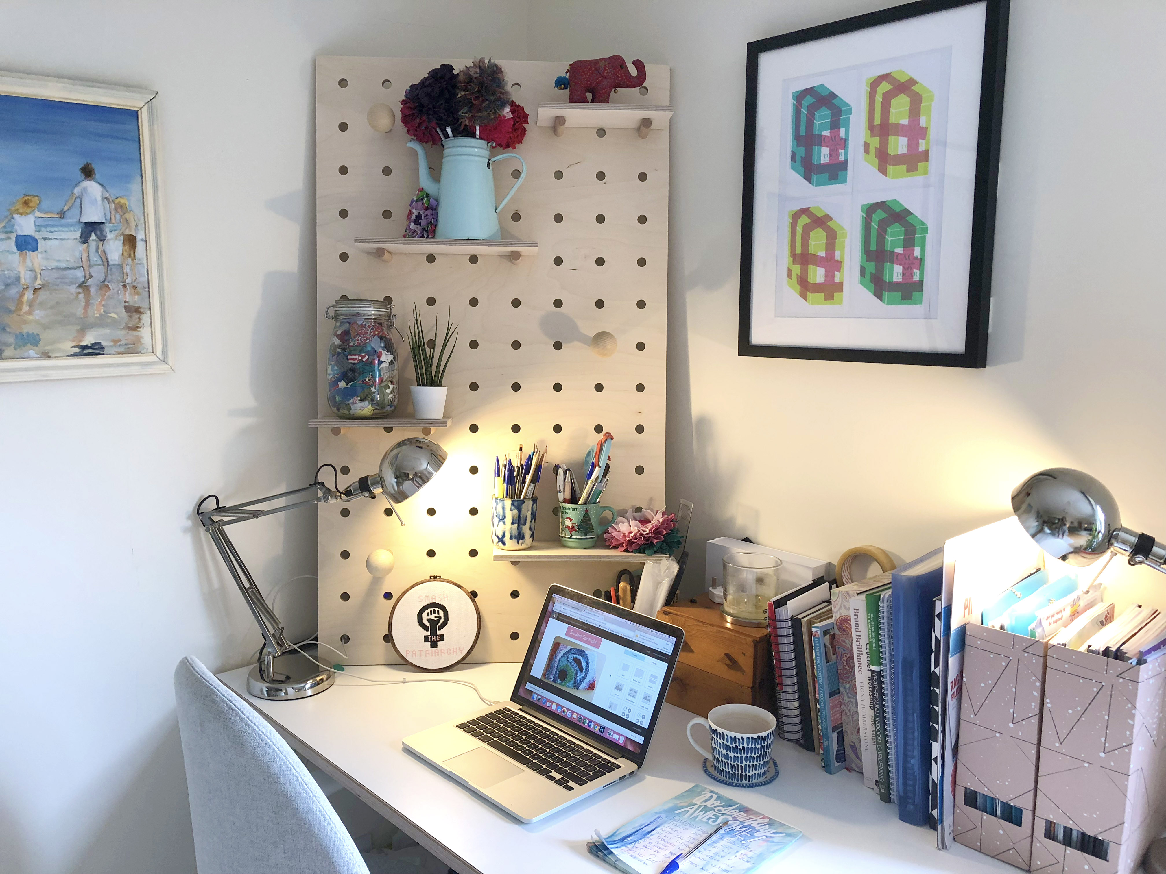 Cute home office with wooden peg board, macbook, art and plants
