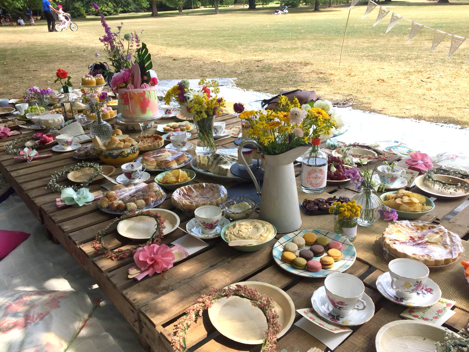 Pallet table outdoor picnic in the park with flowers and afternoon tea cakes