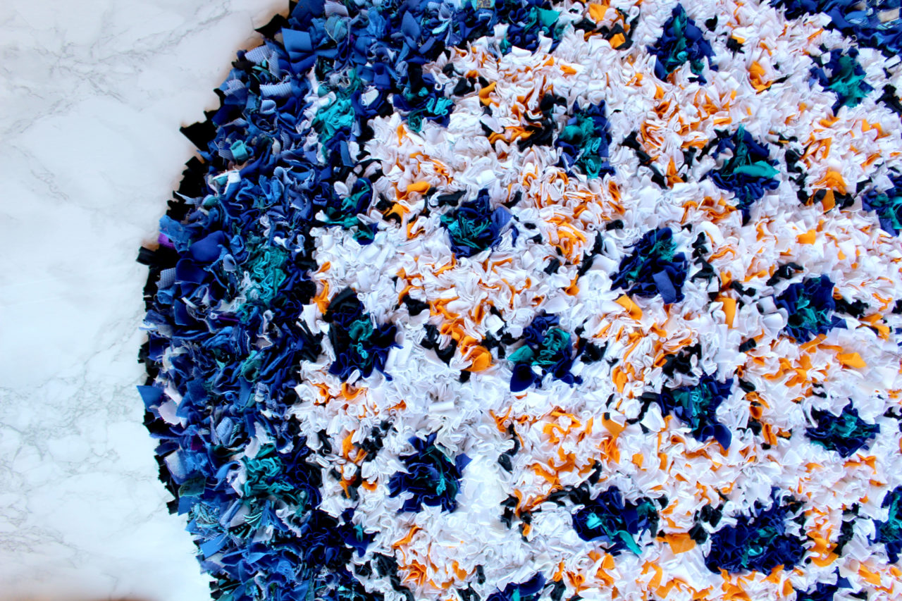 Circular shaggy rag rug in blue, white and orange with triangles of colour