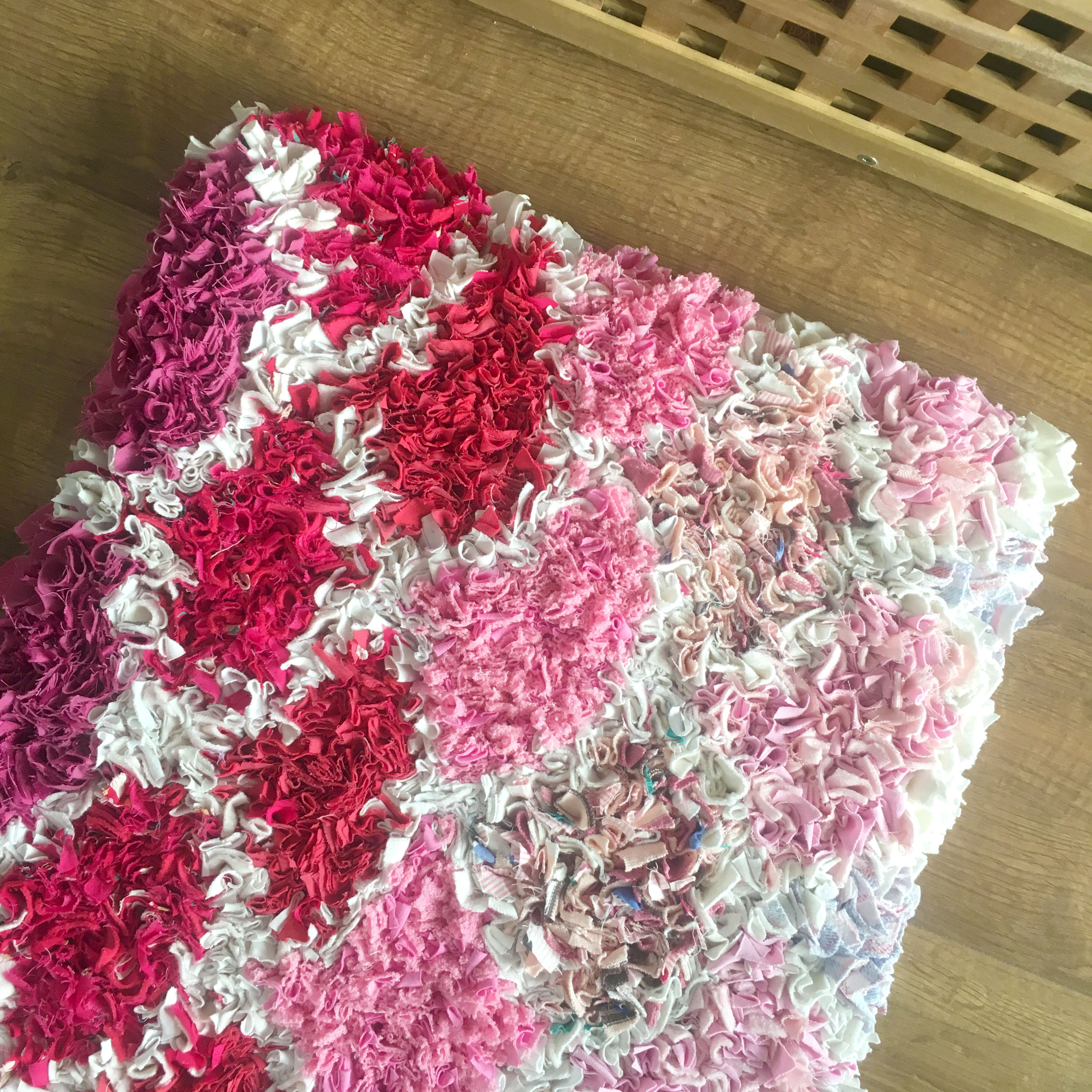Pink rag rug in scallop design with white borders made of old t-shirts