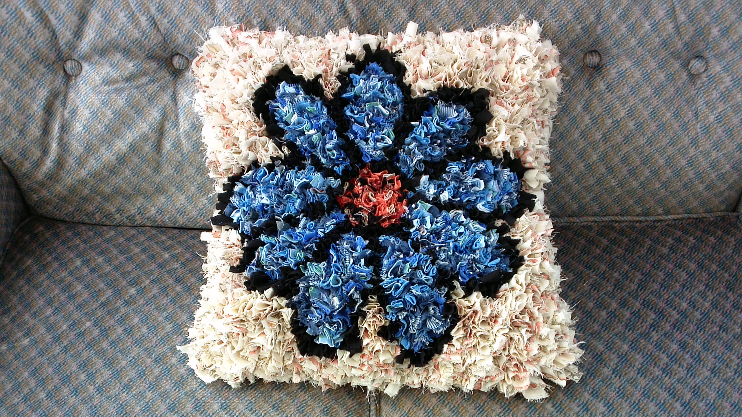 Handmade Blue and Cream Shaggy Rag Rug Cushion on a grey sofa