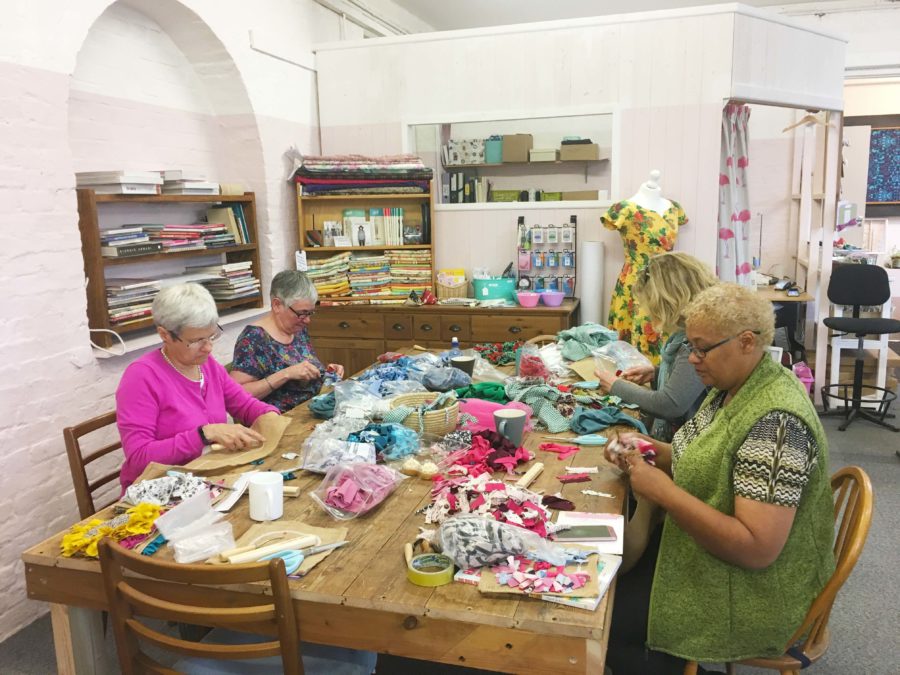 A group of ladies rag rugging at a table in a rag rug workshop at the Craft Space in Wiltshire