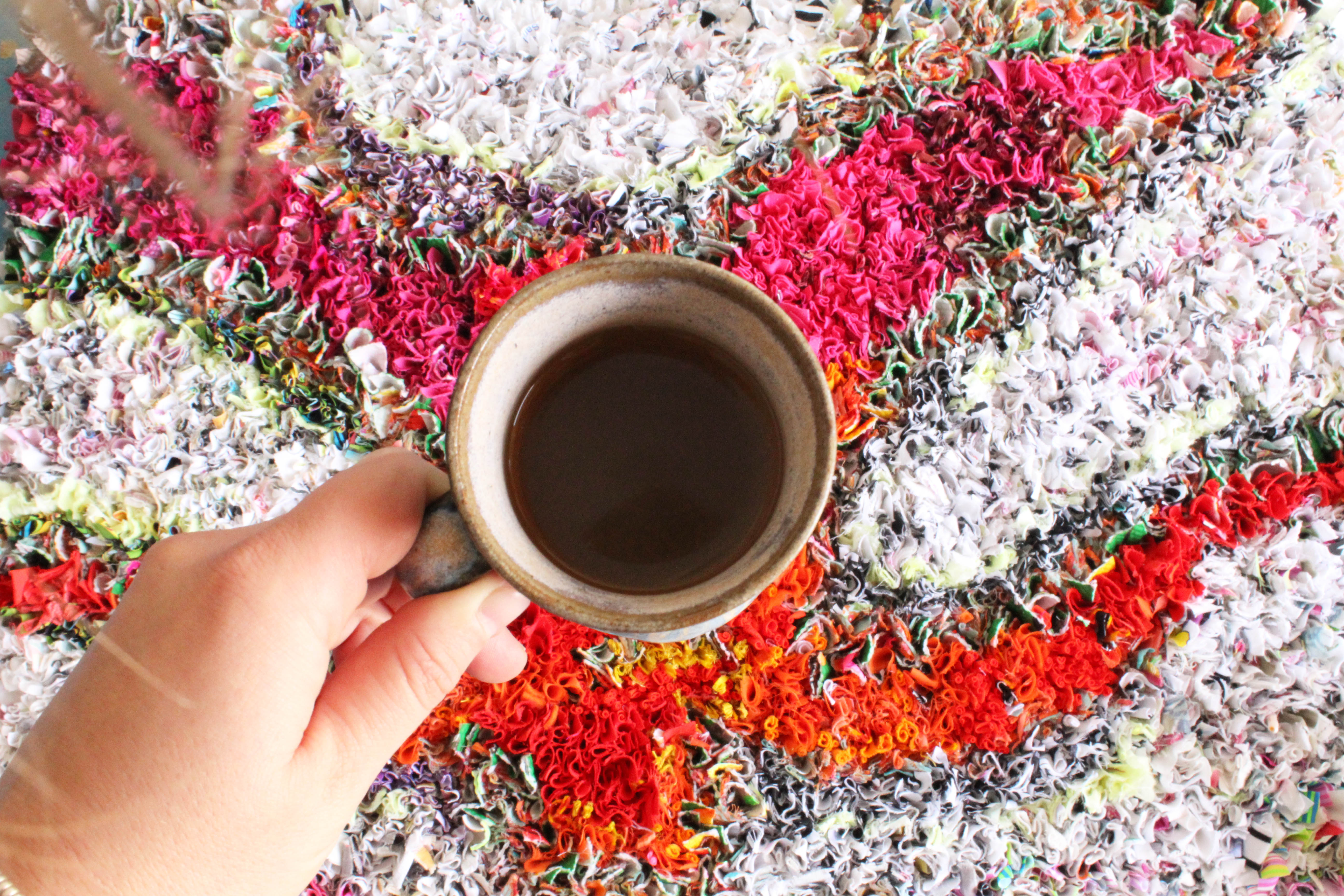 A cup of coffee on top of a colourful shaggy rag rug