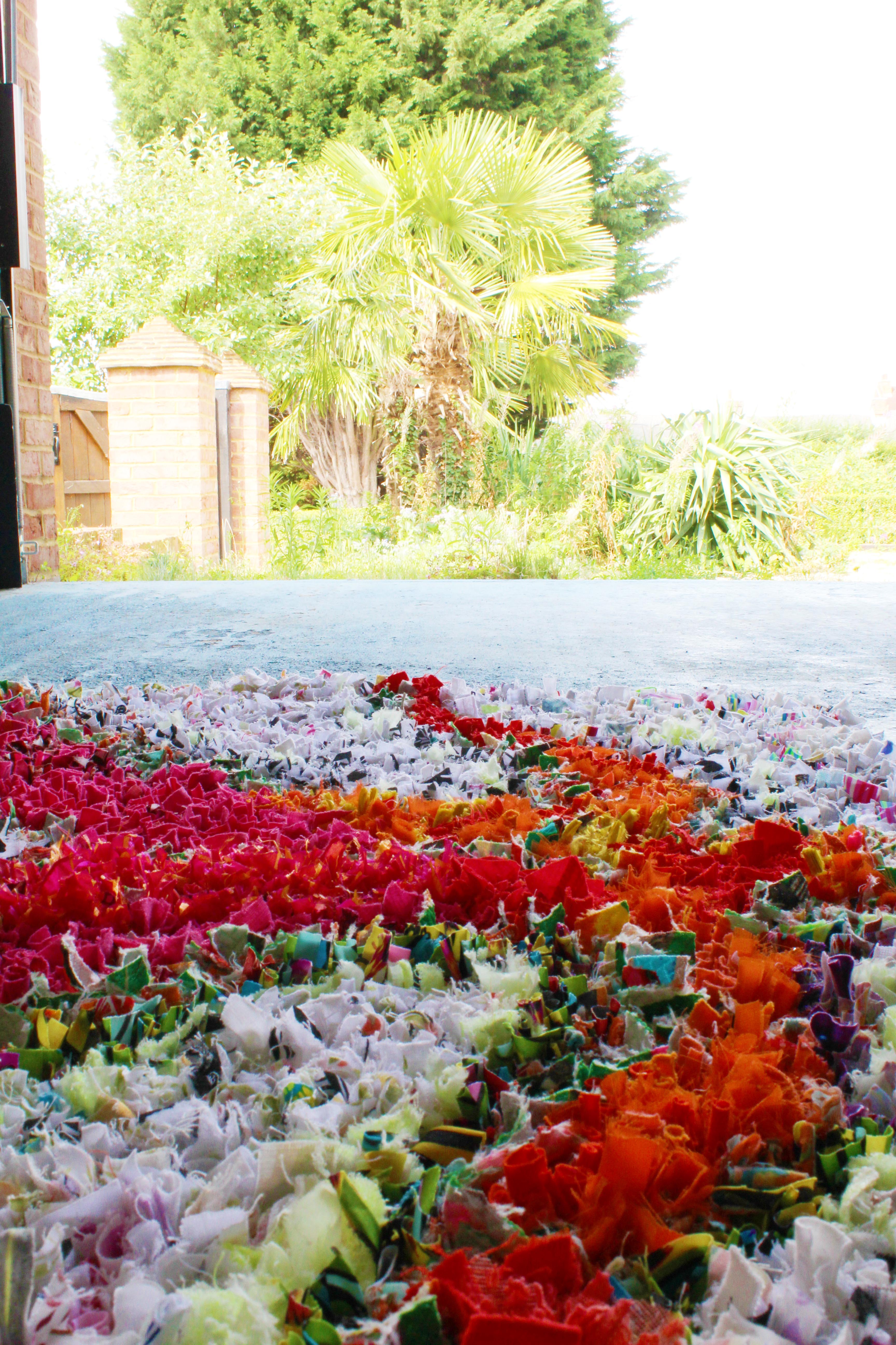 Close up of bright rag rug from the side with trees in the background and a blue floor