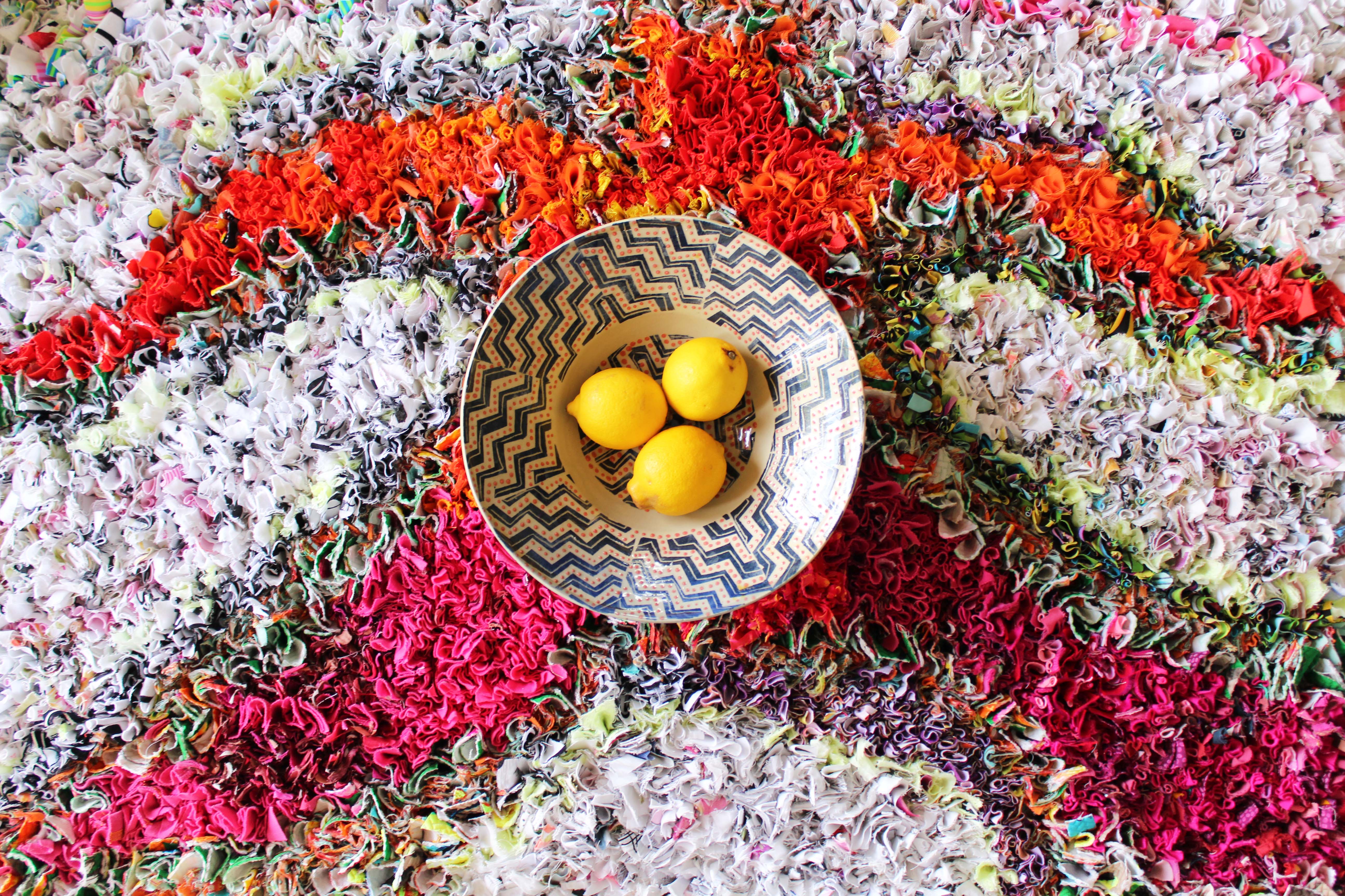 A bowl of yellow lemons in the centre of a finished rag rug 