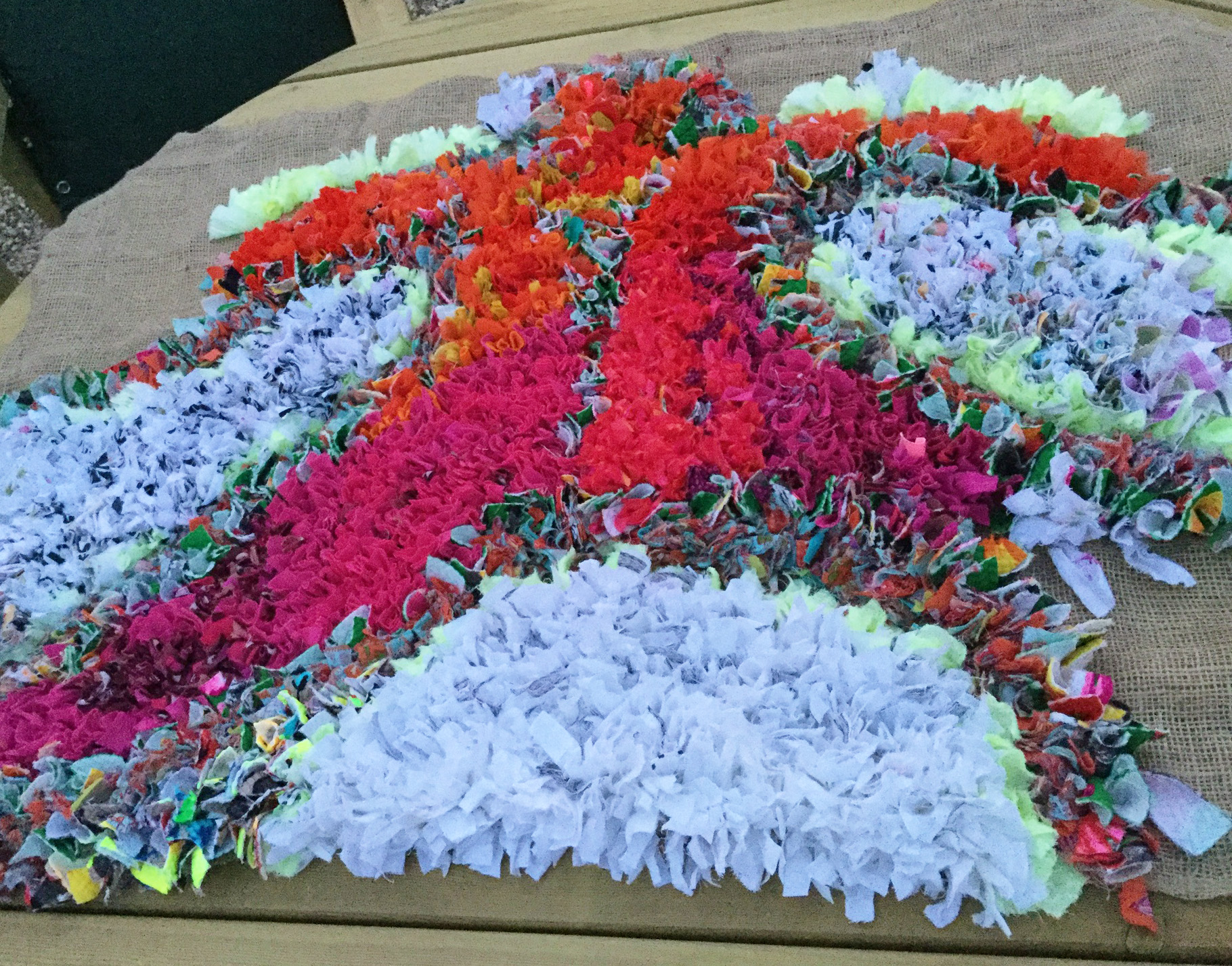 A work in progress photo of a proggy rag rug with white, orange and pink