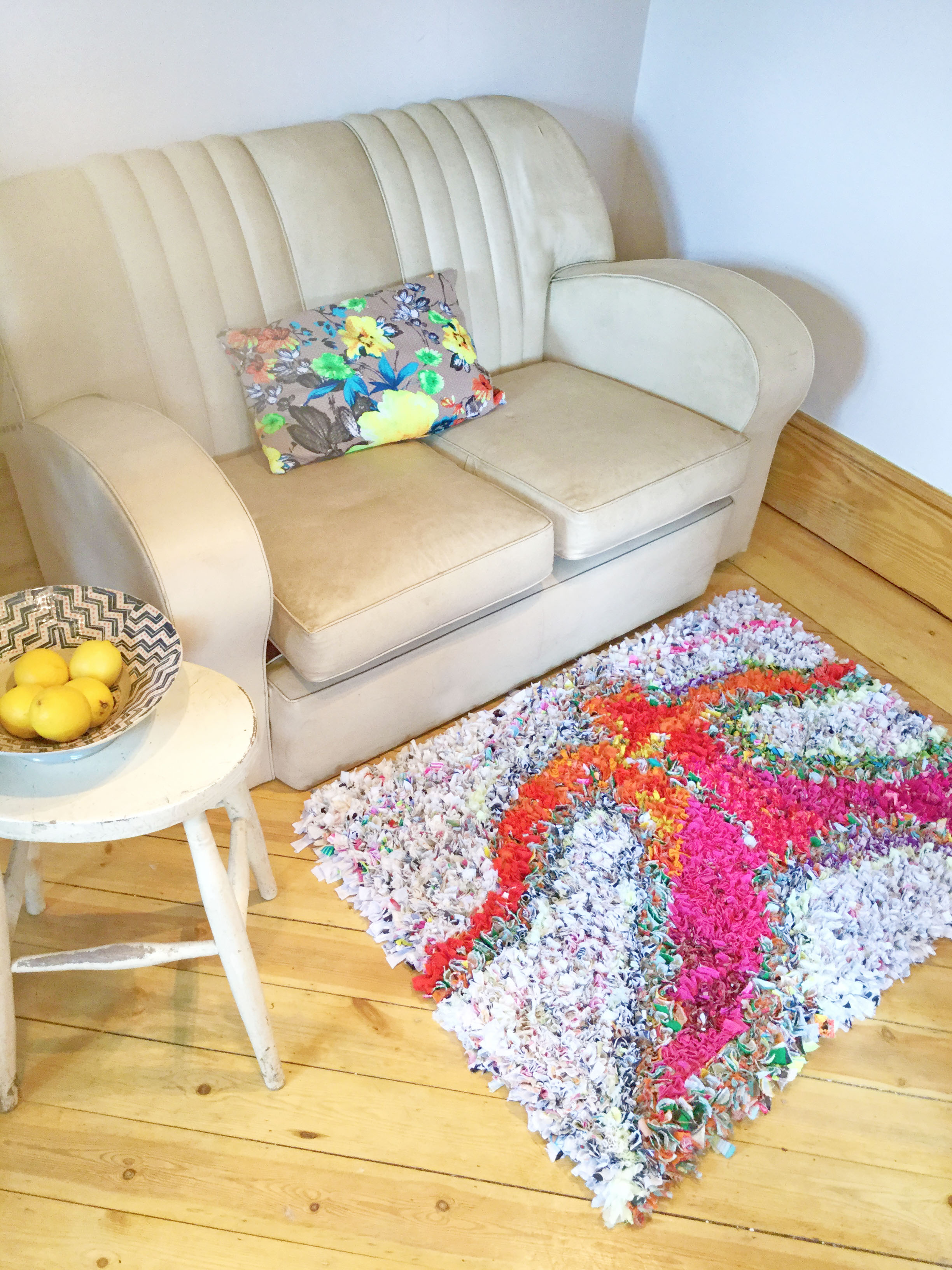 A unique rag rug in front of a white vintage sofa on a wooden floor