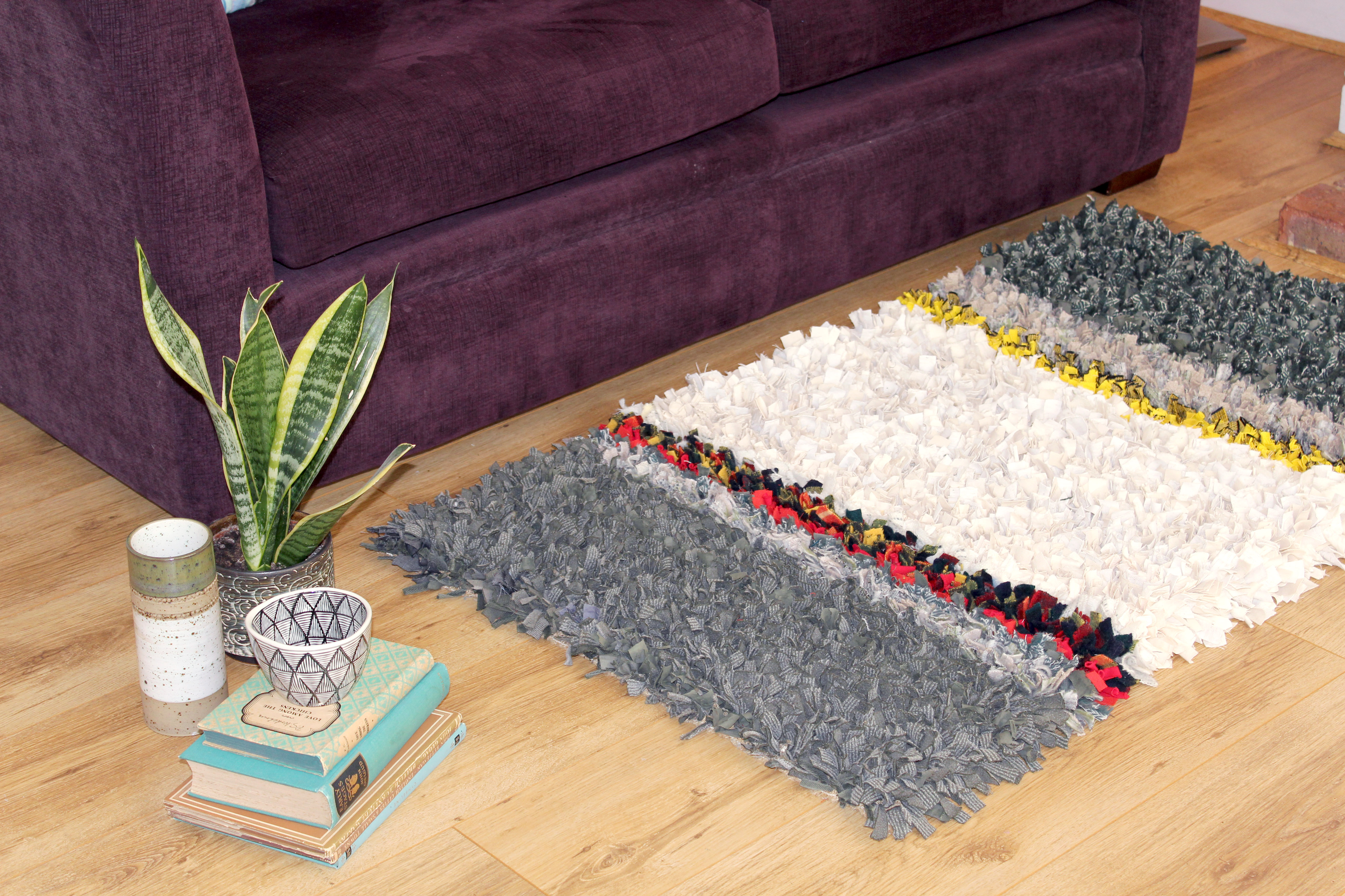 Rag rug made by hand in front of sofa in grey, red, yellow and green colours. 