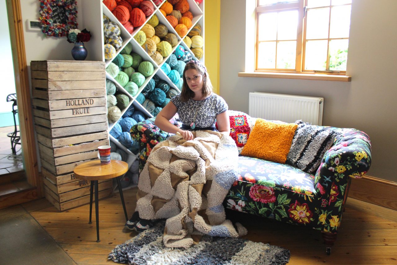Elspeth Jackson from Ragged Life rag rugging on a sofa with rainbow blanket yarn