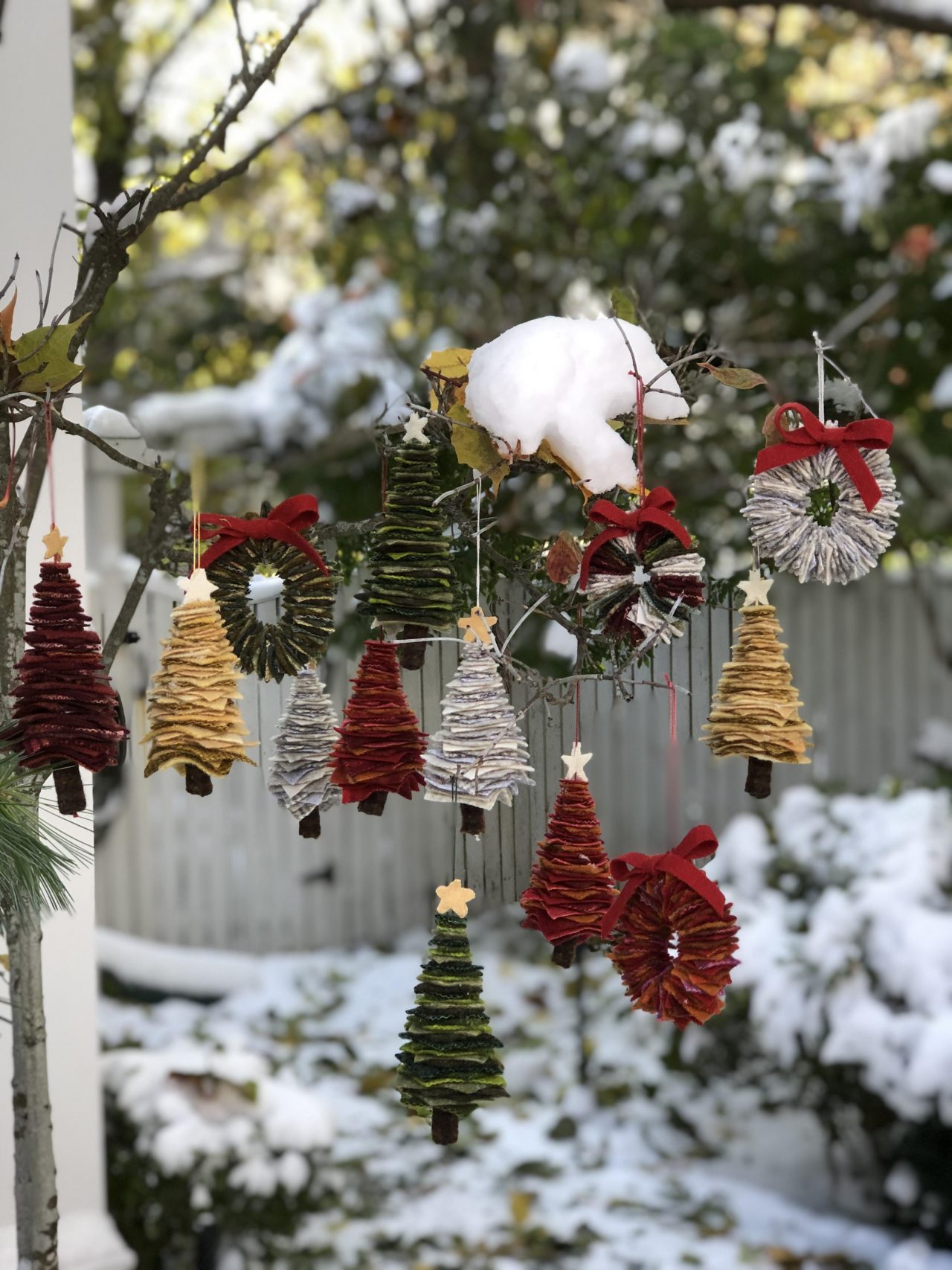 Mini textile christmas tree decorations hanging on a snowy tree by Yvonne Iten-Scott