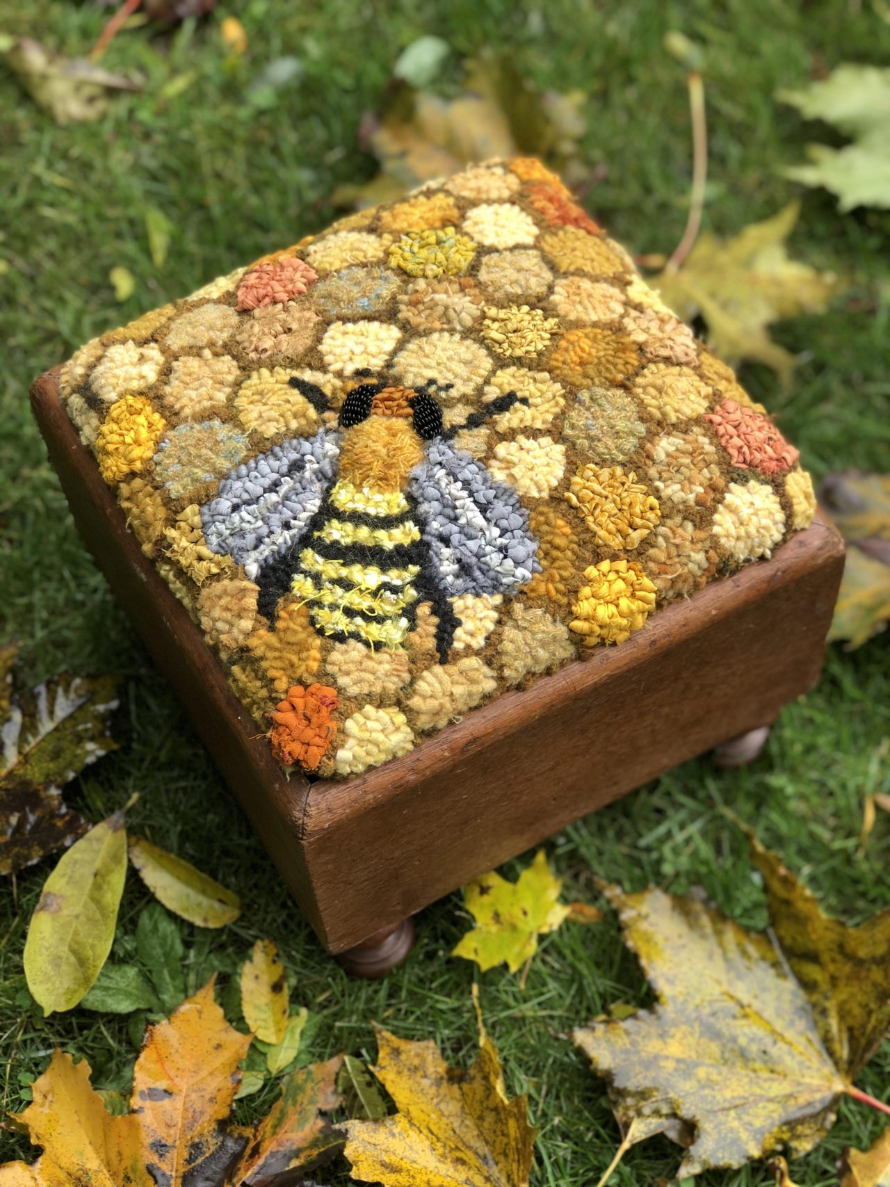A textile art footstool cover featuring honeycomb background and a bee by Yvonne Iten-Scott