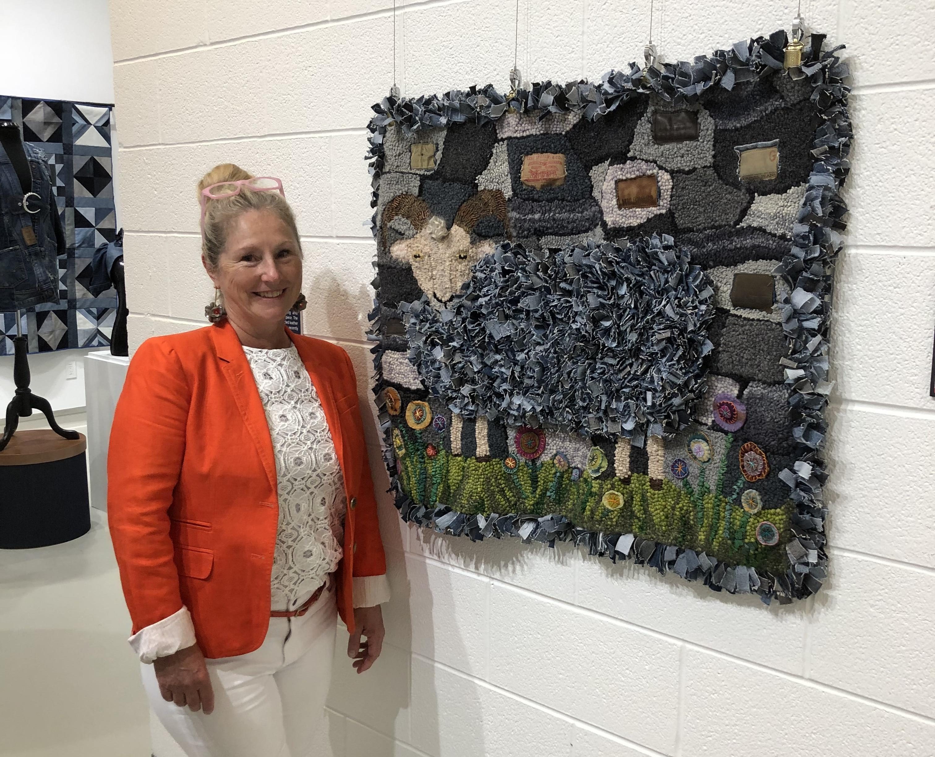 Artist Yvonne Iten-Scott standing by her textile art of a sheep made from denim scraps in a white gallery