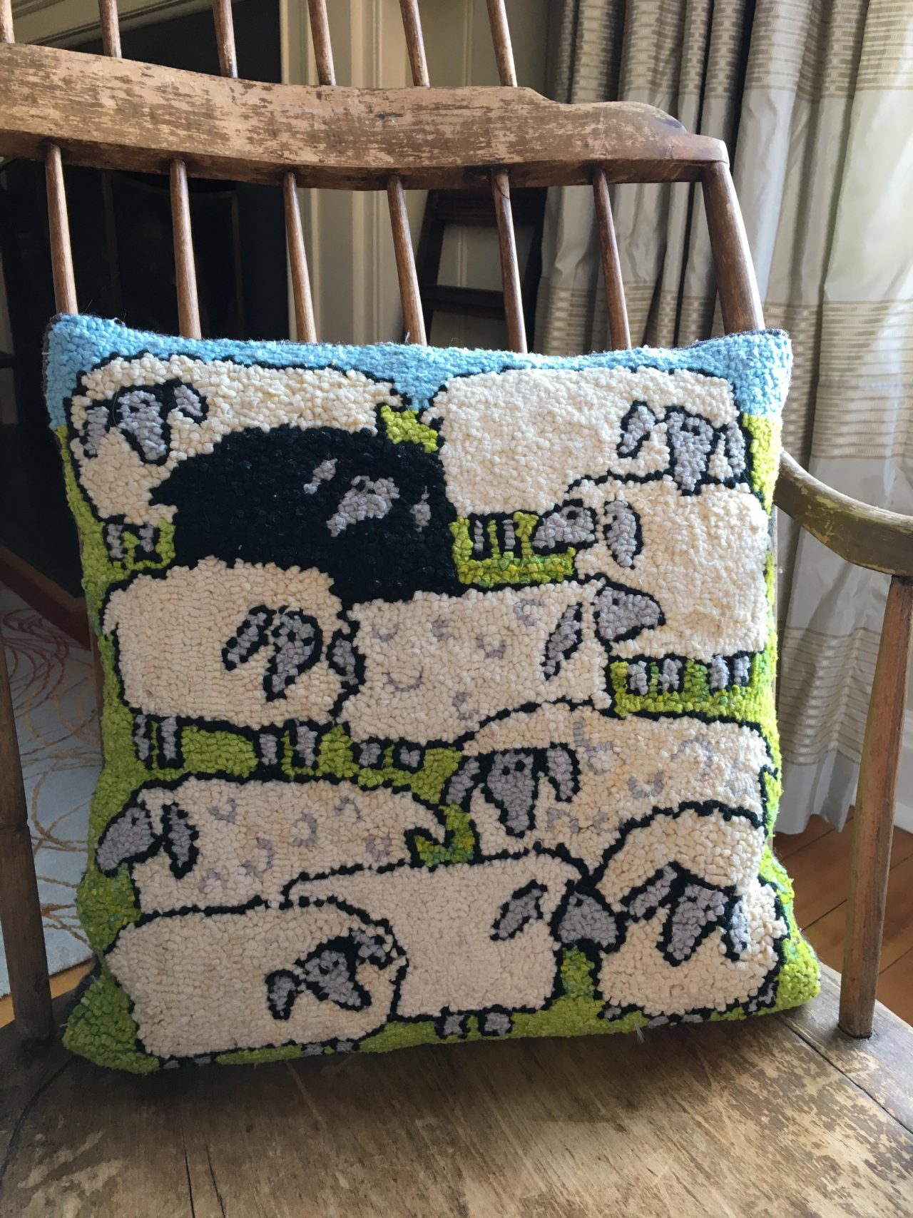A hooked cushion with 10 white sheep and one black sheep on a wooden chair by Yvonne Iten-Scott.