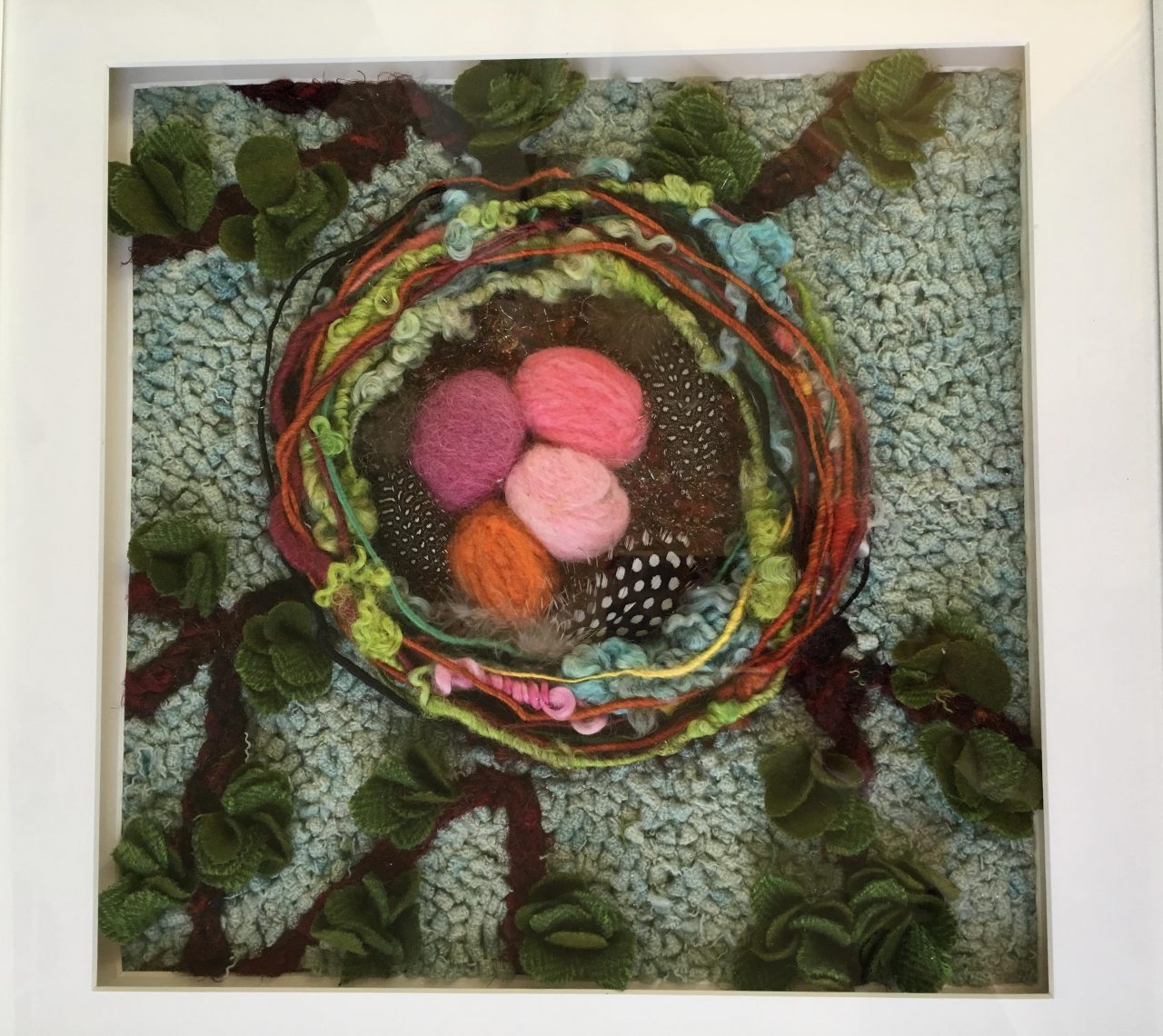 A hooked piece of textile art featuring a colourful birds nest on a green background by Yvonne Iten-Scott.