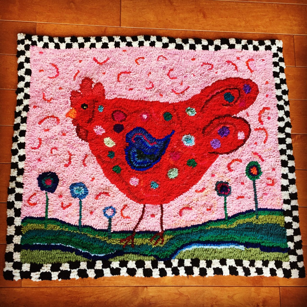 Textile art of a red hen on a pink background with a checkerboard edging by Yvonne Iten-Scott