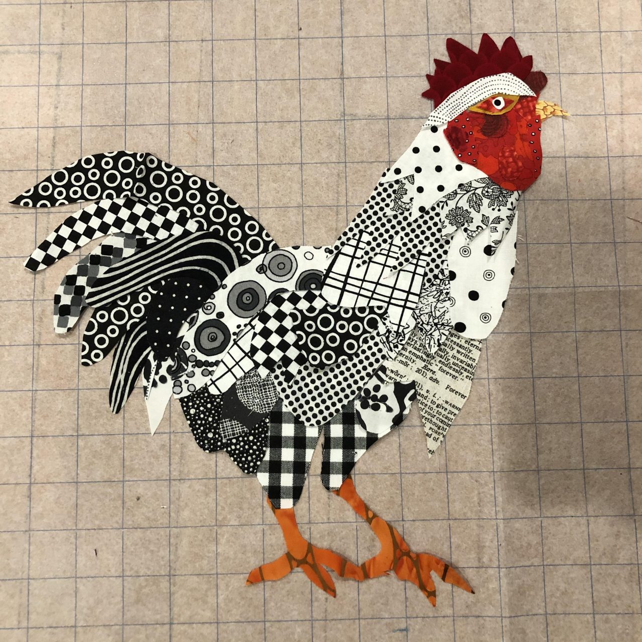 An applique cockerel with a black and white patterned body, orange feet and a red face by Yvonne Iten-Scott. 
