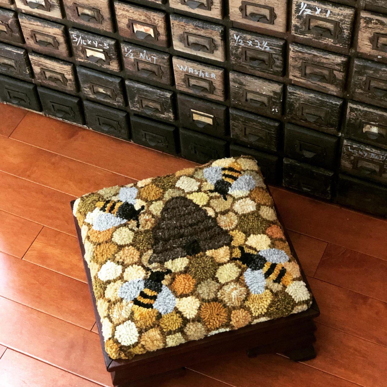 A textile art footstool cover with honeycomb background, 4 bees and a hive in the middle by Yvonne Iten-Scott