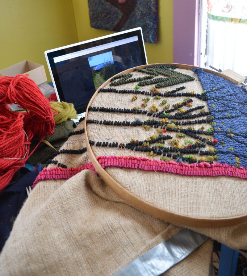 An embroidery hoop with hooked wool patterns in blue, pink and grey by Laura Kenney.