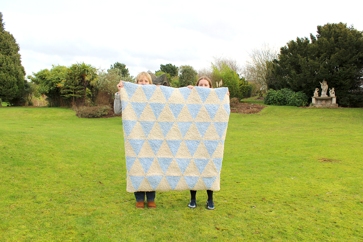 Women holding up large blue and cream triangle rag rug