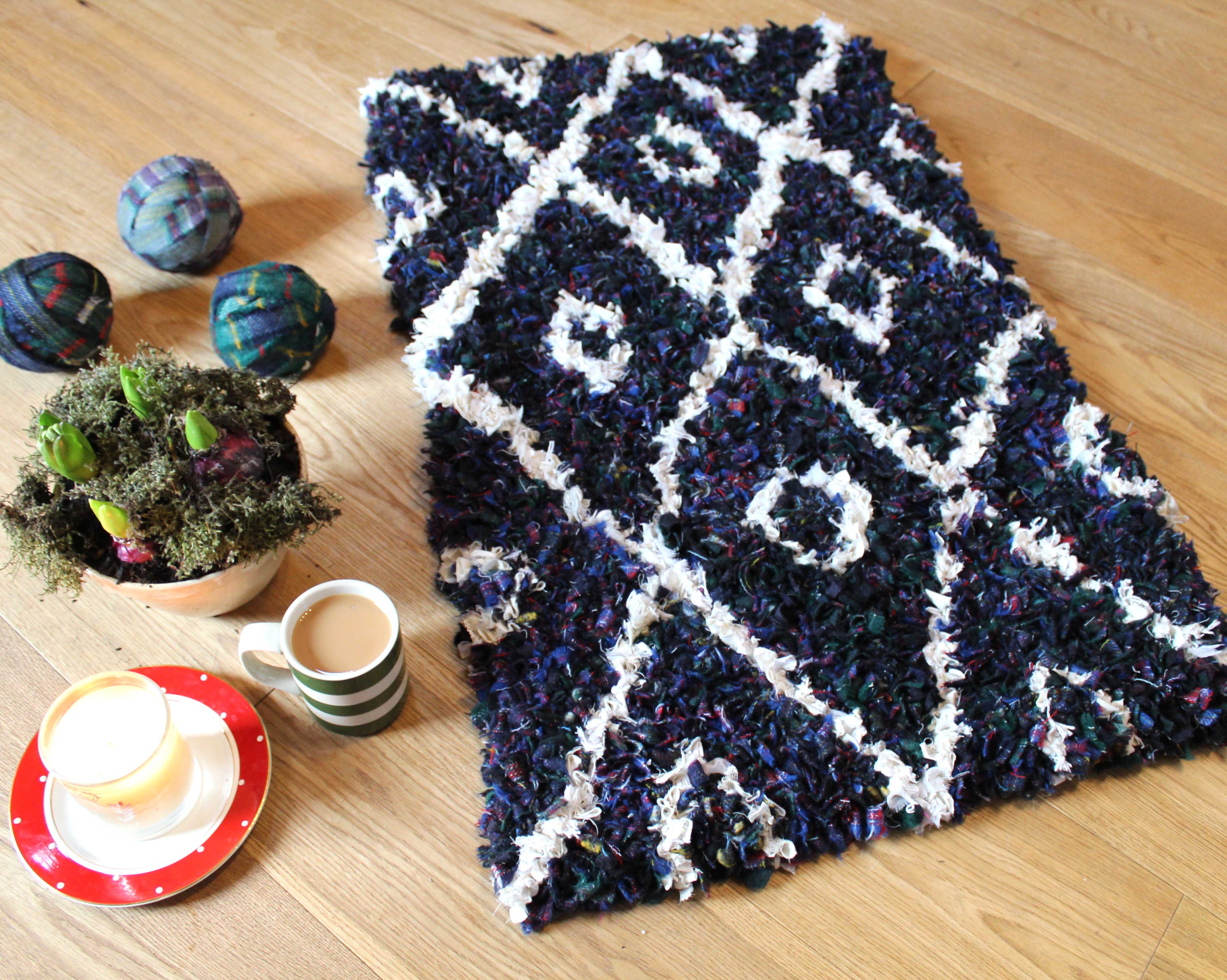 two tone rug next to balls of blanket yarn and cup of tea