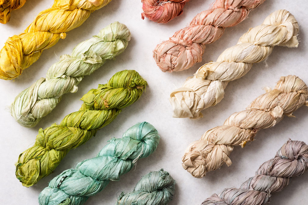 Ragged Life recycled sari silk ribbon skeins arranged in rainbow order in pink, blue, green, cream, grey and duck egg blue. 